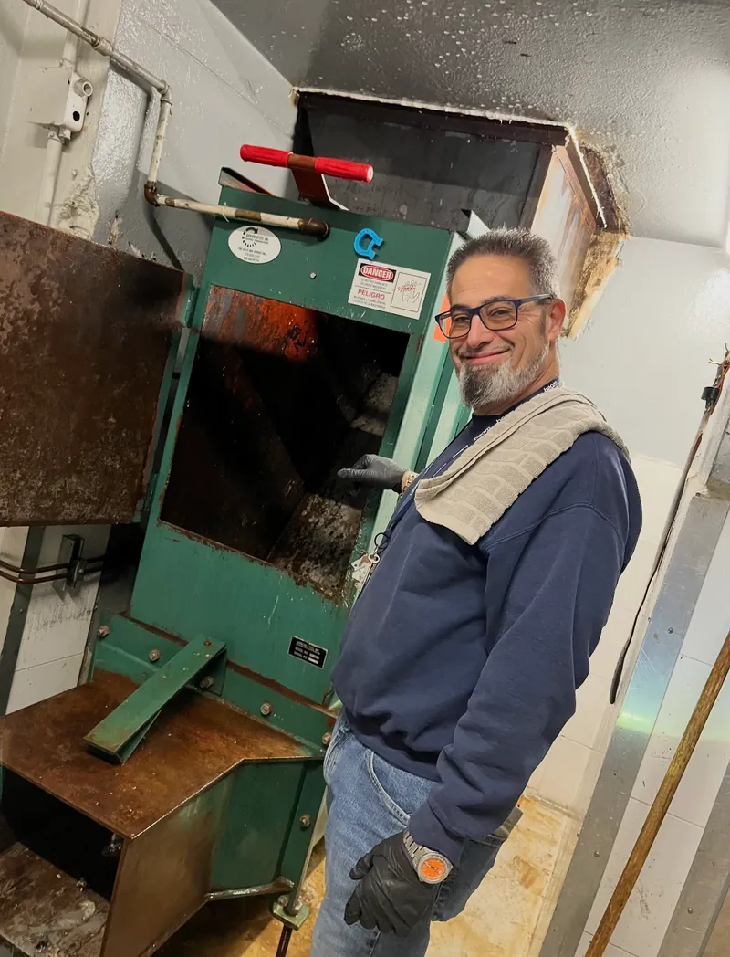 Marshall, founder of Chute Cleaning Division, smiling beside a trash chute hopper in a building's compactor room.